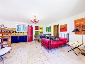 A room with a bed, a dining table, a kitchen area, and a chandelier. - Villa Vivaris (VEN111) by Interhome (Vence)