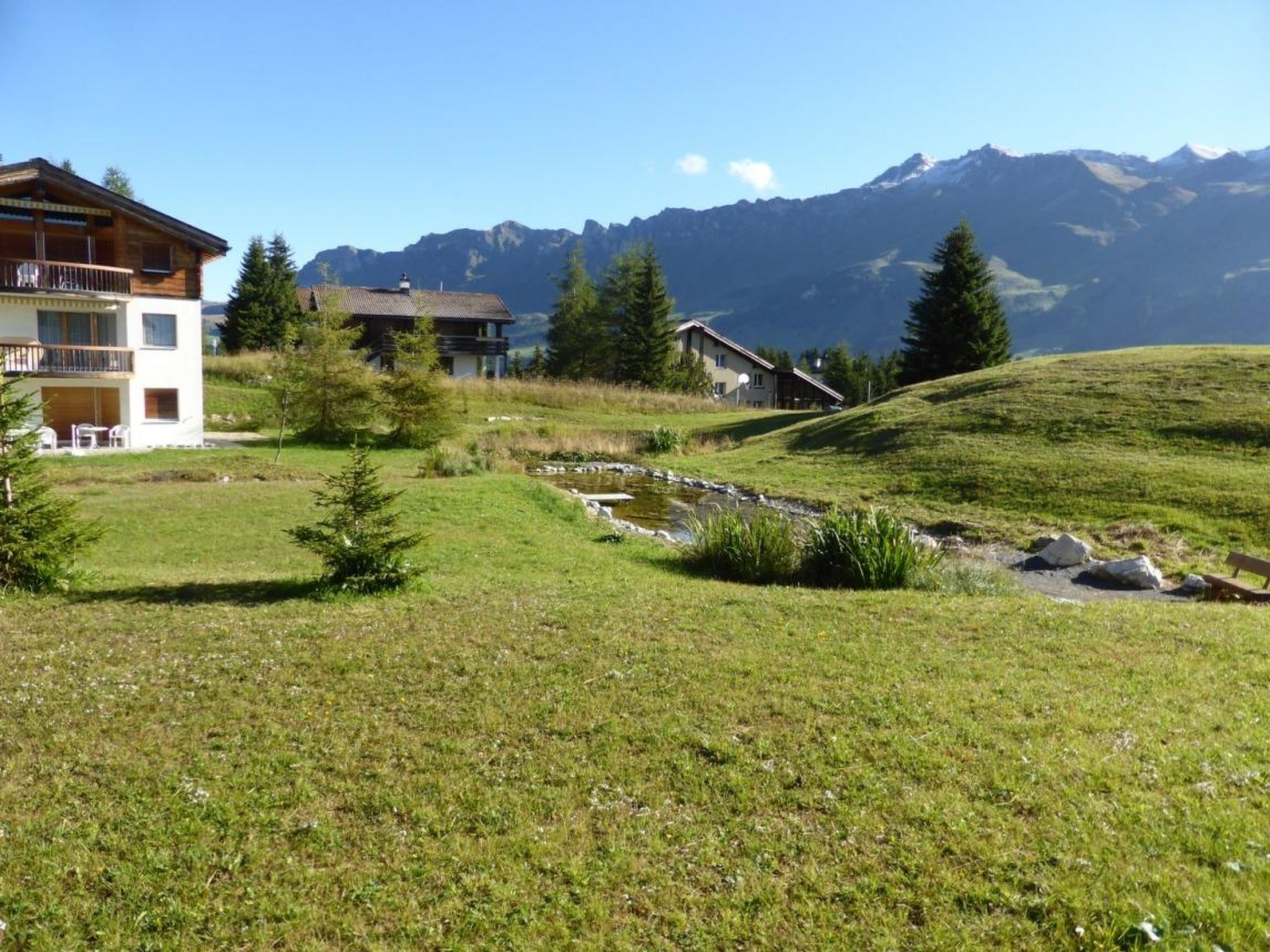Ein Hang mit einem kleinen Bach, einem Holzhaus und einem Gebäude mit einem Balkon.
