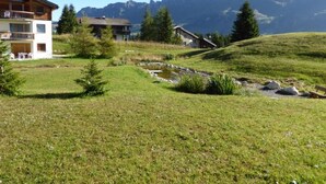 Une colline avec un petit ruisseau, une maison en bois et un bâtiment doté d’un balcon.