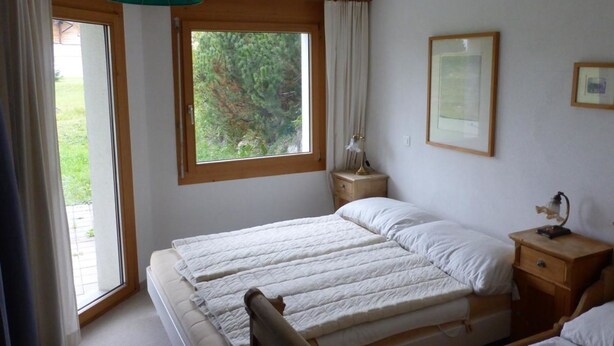 Une chambre à coucher comprenant un lit, une table de chevet, une commode, une fenêtre et un luminaire suspendu.