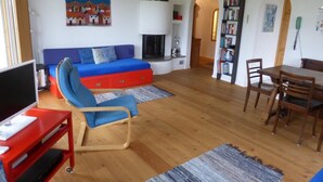 Un salon avec un canapé bleu, un meuble de télévision rouge, une cheminée et un coin repas comprenant une table et des chaises en bois.