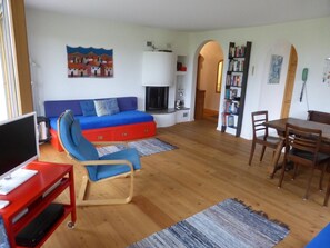 A living room with a blue sofa, a red entertainment unit, a fireplace, and a dining area with a wooden table and chairs. - Cresta Sartons Brenn Appartement/Fewo, Badewanne, 1 Schlafraum by Interhome (Valbella)