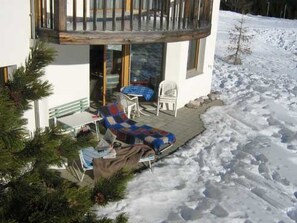 A residential building with a balcony, a covered outdoor seating area, and a snow-covered ground. - Cresta Sartons Brenn Appartement/Fewo, Badewanne, 1 Schlafraum by Interhome (Valbella)