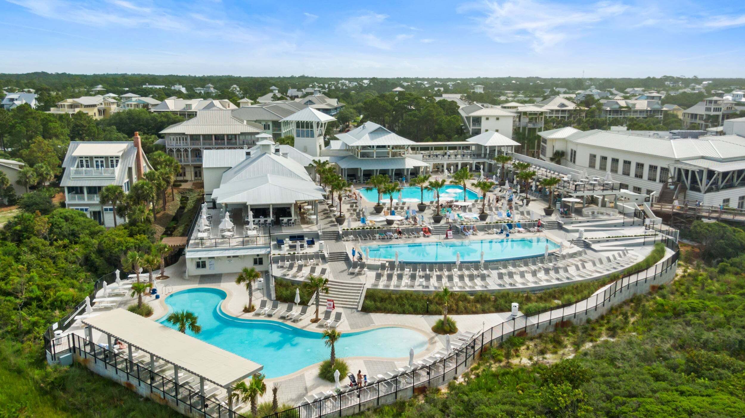A resort with multiple swimming pools, lounge areas, and a view of the surrounding neighborhood.