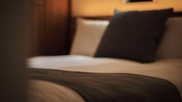 Una cama con sábana blanca y almohada oscura en una habitación con paredes de madera y un cuadro en la pared.