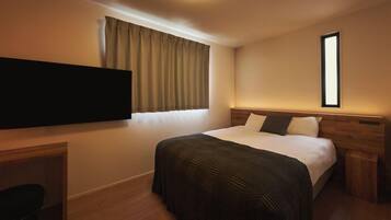 A hotel room with a bed, a television mounted on the wall, a desk, and a window with curtains.