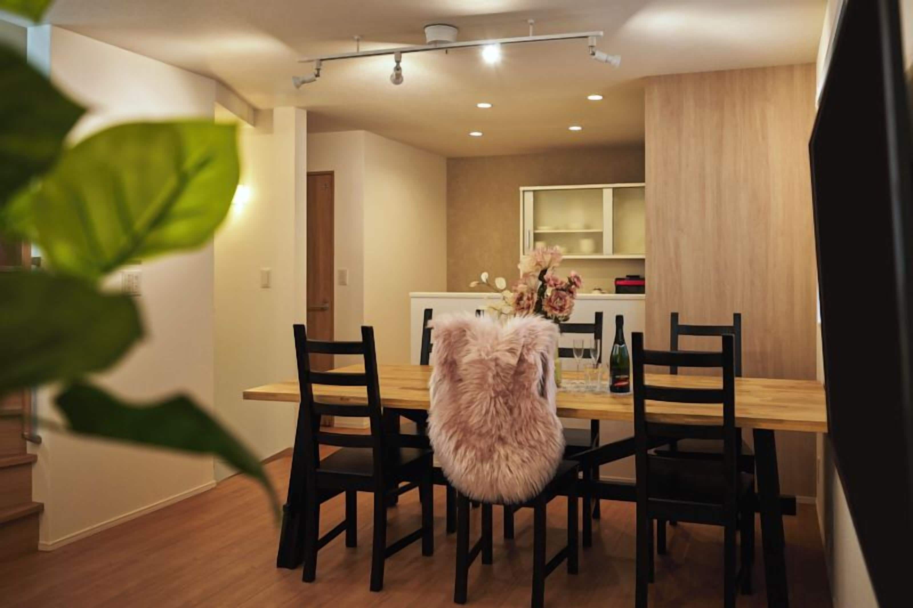 Un comedor con una mesa y sillas de madera, un sillón mullido y una cocina al fondo.