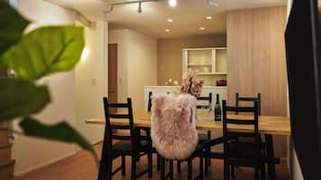 Un comedor con una mesa y sillas de madera, un sillón mullido y una cocina al fondo.