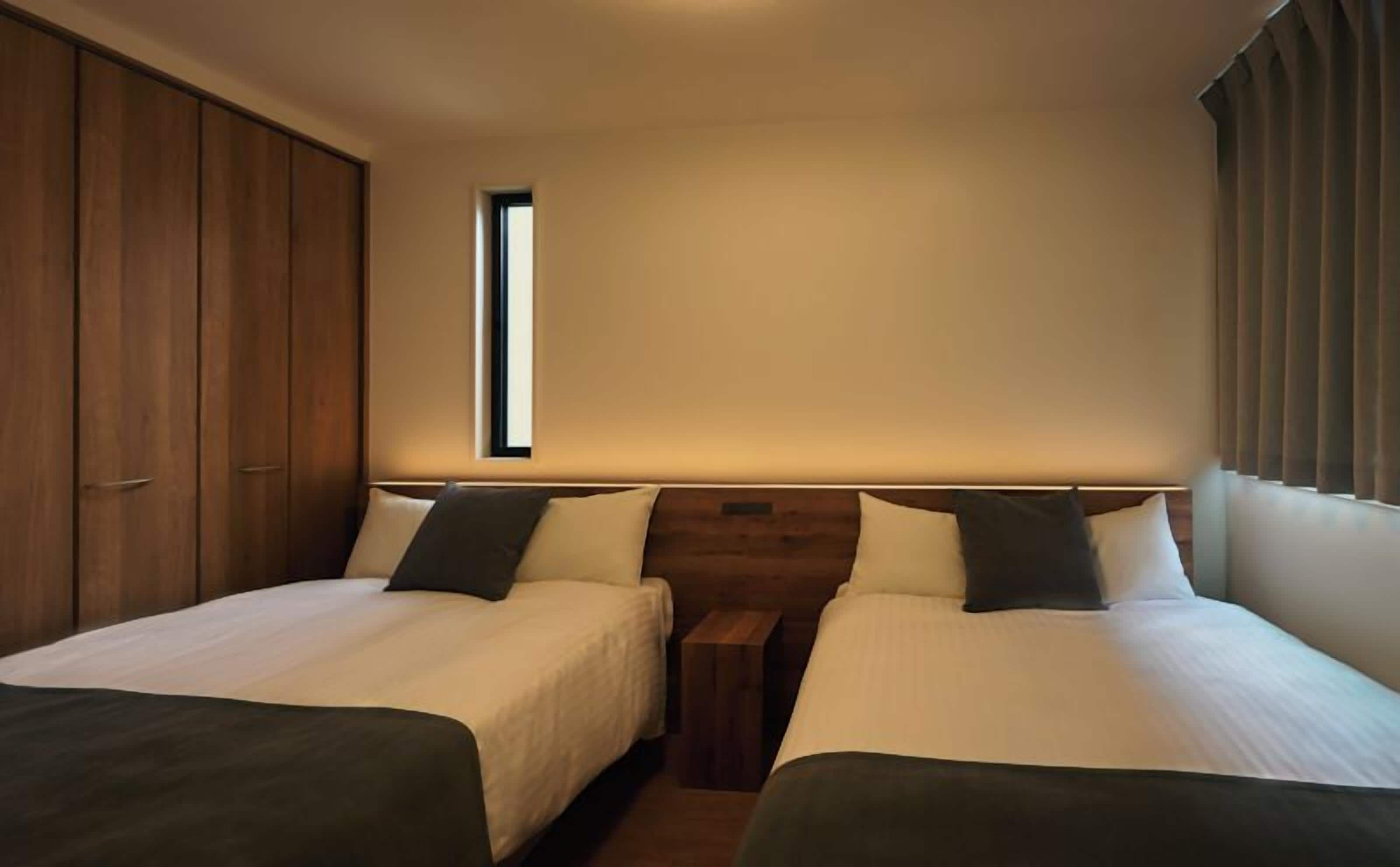 Una habitación de hotel con dos camas, un armario y una ventana.