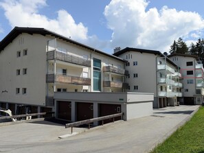 A multi-story residential building with balconies, a garage area, and a clear sky. - Haus Montana 3/6 Appartement/Fewo,   4-Bettwohnung by Interhome (Lenzerheide)