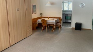 Een kleine keuken met een kookplaat en oven, een eethoek met tafel en stoelen, en een grote inbouwkast.
