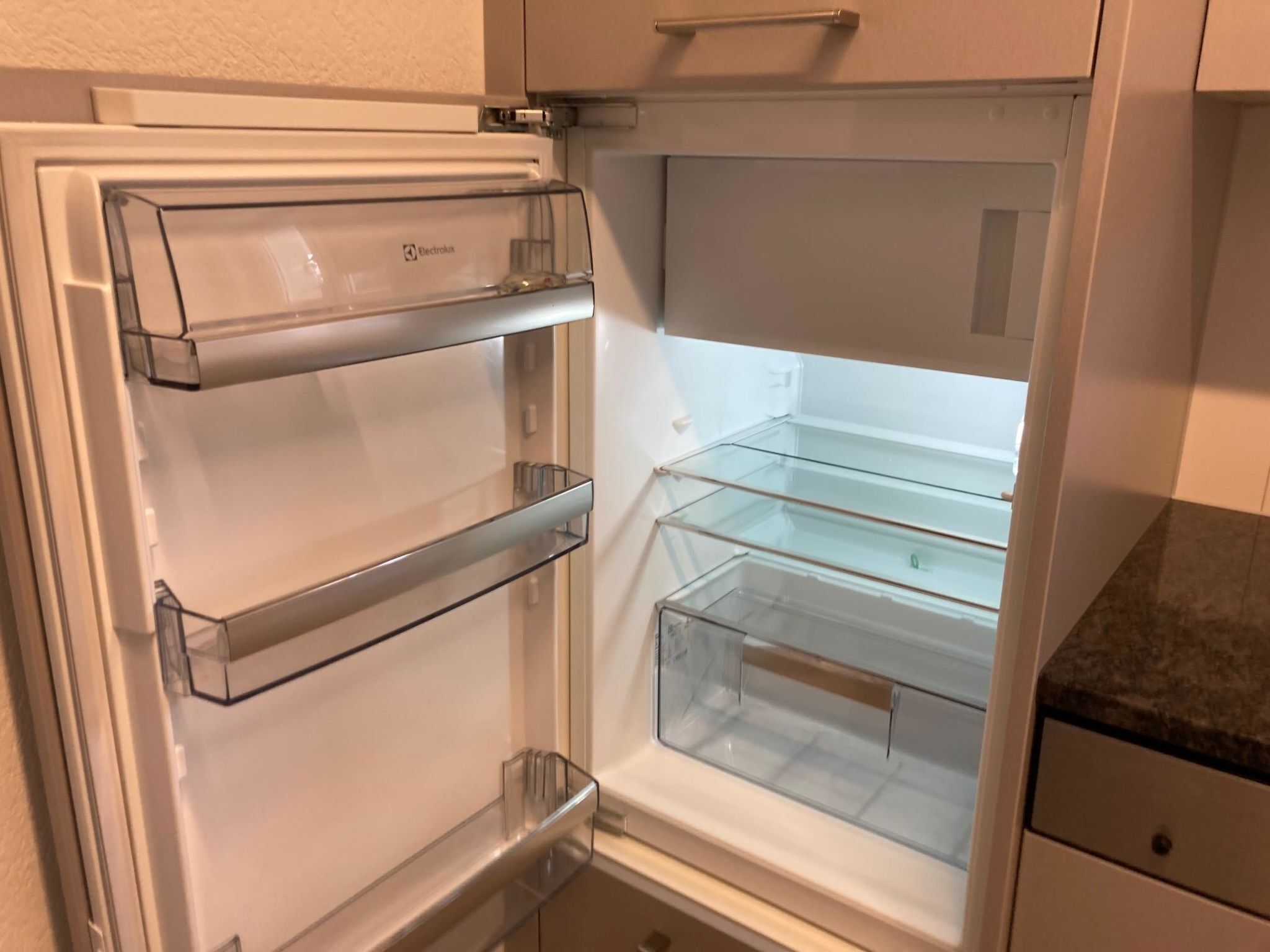 Un refrigerador abierto con estantes transparentes y un compartimento de puerta de vidrio.