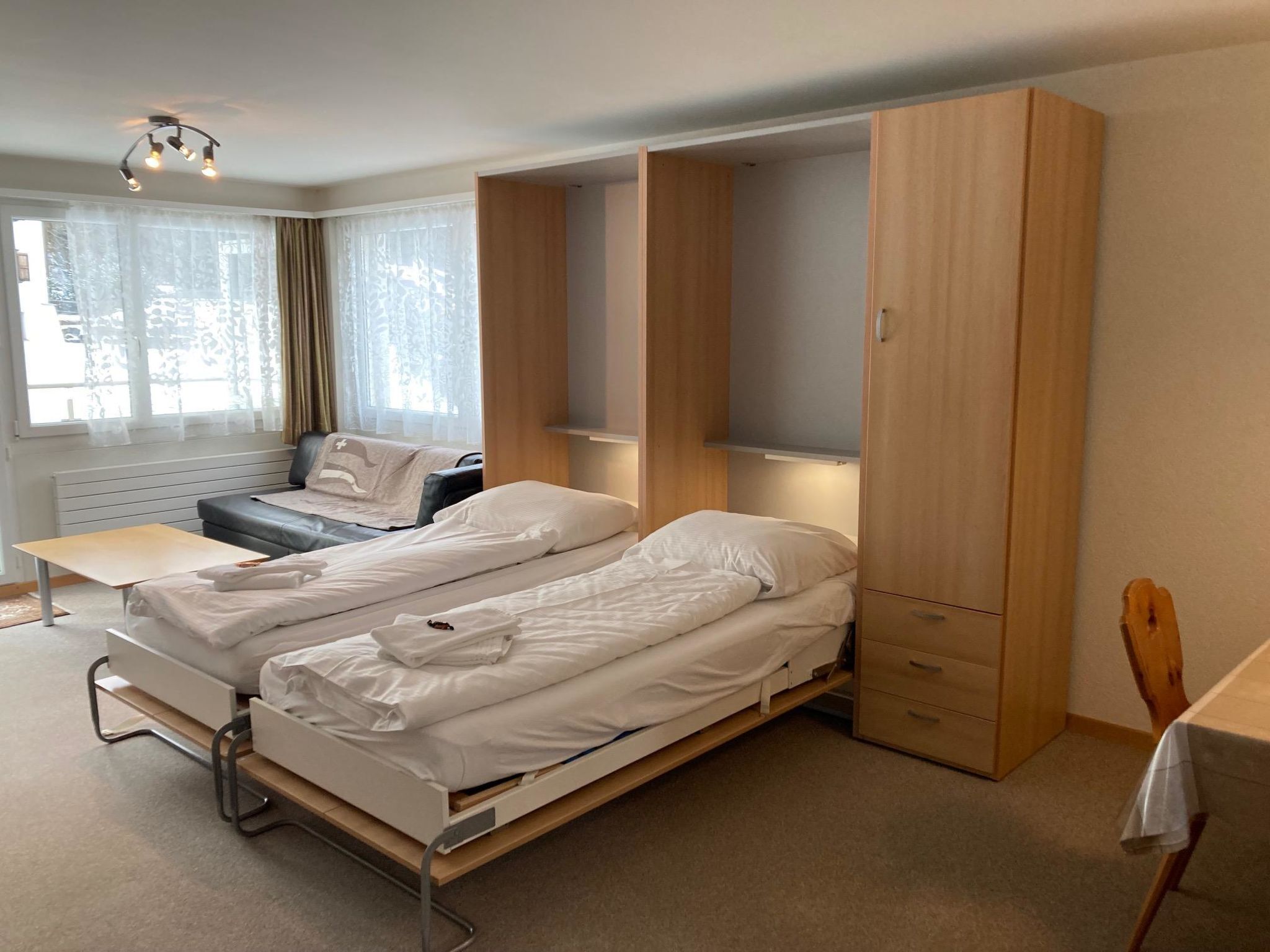 Habitación de hotel compacta con dos camas individuales, un escritorio, una silla y un armario.