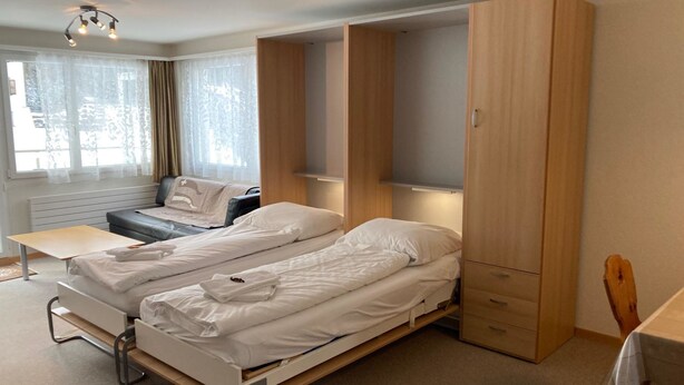 Een compacte hotelkamer met twee eenpersoonsbedden, een bureau, een stoel en een kledingkast.