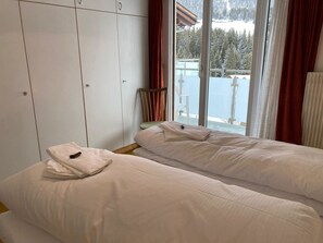 Ein Schlafzimmer mit zwei Betten, einem Kleiderschrank und einem Fenster mit Blick auf eine verschneite Landschaft.