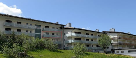 Un immeuble à plusieurs étages, doté de balcons, entouré de verdure et surplombant un ciel dégagé.