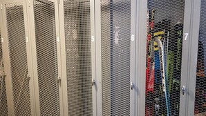 Een rij van zes genummerde metalen lockers met gaasdeuren, waarschijnlijk voor opslag.