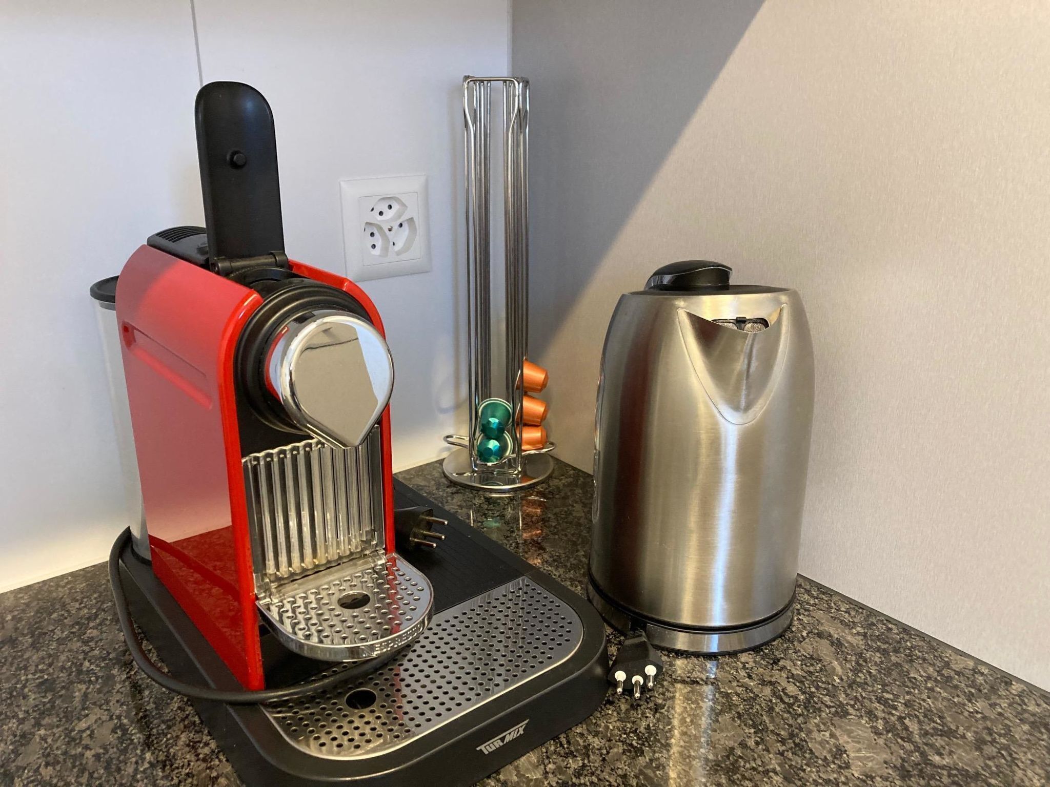 Eine Kaffeemaschine mit roter Basis und einem Edelstahl-Wasserbehälter auf einer Granitabdeckung.