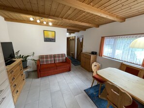 Ein gemütliches Zimmer mit Holzboden, einer Couch, einem Esstisch und einem Fernseher.