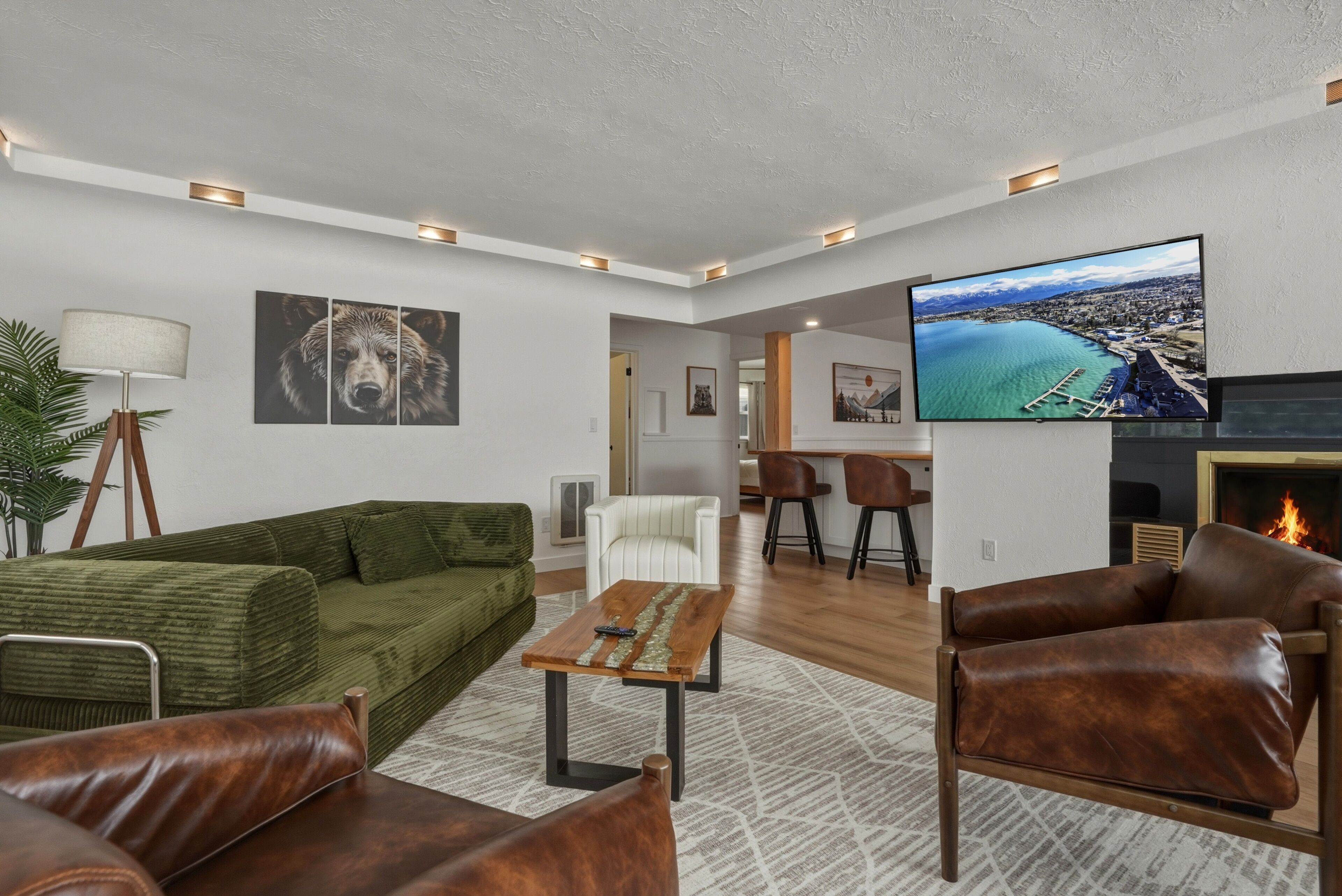 A modern living room with a green sofa, leather armchairs, a coffee table, a TV, and a fireplace.