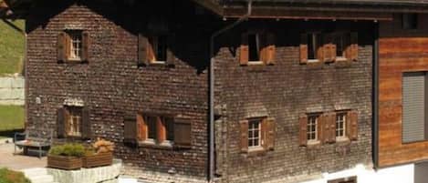 Un chalet rustique avec une façade en pierre, des volets en bois et un toit en pente.