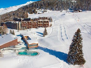 A ski resort with a large building complex, a snow-covered slope, and a pool area.