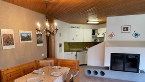 A dining area with a wooden table set for four, a chandelier, and a kitchen in the background. - Soleval Tavanera 118 Moritz Appartement/Fewo,   5-Bettwohnung (3 Zimmerwohnung) by Interhome (Lenzerheide)