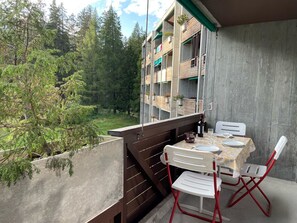 A balcony with a table and chairs, overlooking a forested area.