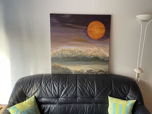 Una habitación con un sofá de cuero negro, un cuadro de un paisaje con luna, y una lámpara de pie blanca.