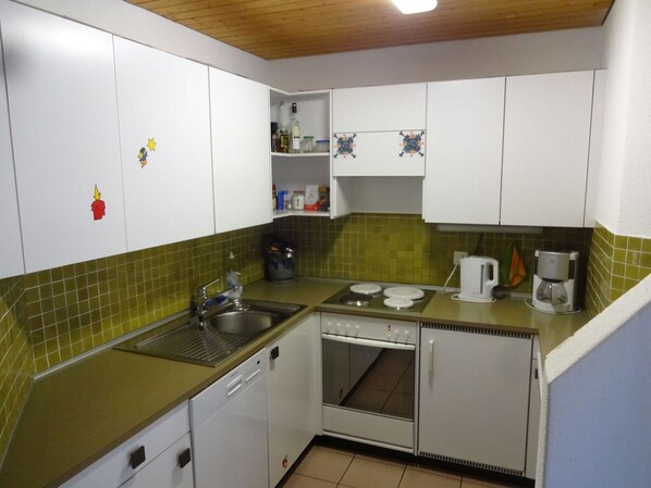 A compact kitchen with white cabinets, a green countertop, a sink, a stove, and a coffee maker.