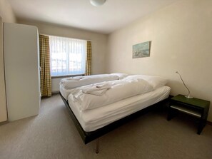 A single bed with white bedding in a room with a window, a painting on the wall, and a small bedside table. - Haus Montana 1/9 Appartement/Fewo,   5-Bettwohnung by Interhome (Lenzerheide)