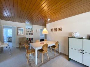 A dining area with a white table, wooden chairs, a hanging light fixture, and a bookshelf with books. - Haus Montana 1/9 Appartement/Fewo,   5-Bettwohnung by Interhome (Lenzerheide)