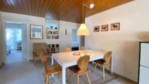 Un comedor con una mesa blanca y sillas de madera, una estantería y una lámpara en el techo.