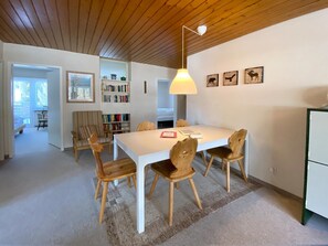 A dining area with a white table and wooden chairs, a bookshelf, and a ceiling light. - Haus Montana 1/9 Appartement/Fewo,   5-Bettwohnung by Interhome (Lenzerheide)