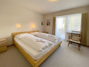 Une chambre à coucher avec un lit en bois, une table de chevet, une chaise et une fenêtre avec des rideaux.