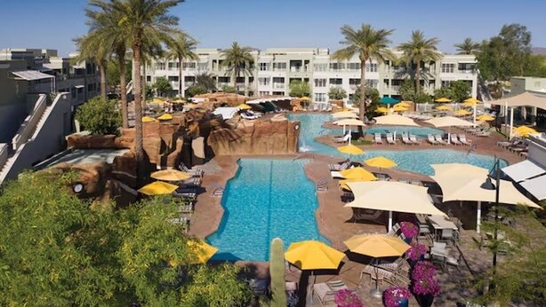 A resort with a central pool, multiple lounge areas with umbrellas, palm trees, and a multi-story building in the background. - 2BR/2BA Villa w/ Pools & Splash Pad – Marriott Canyon Villas, Phoenix (Phoenix)