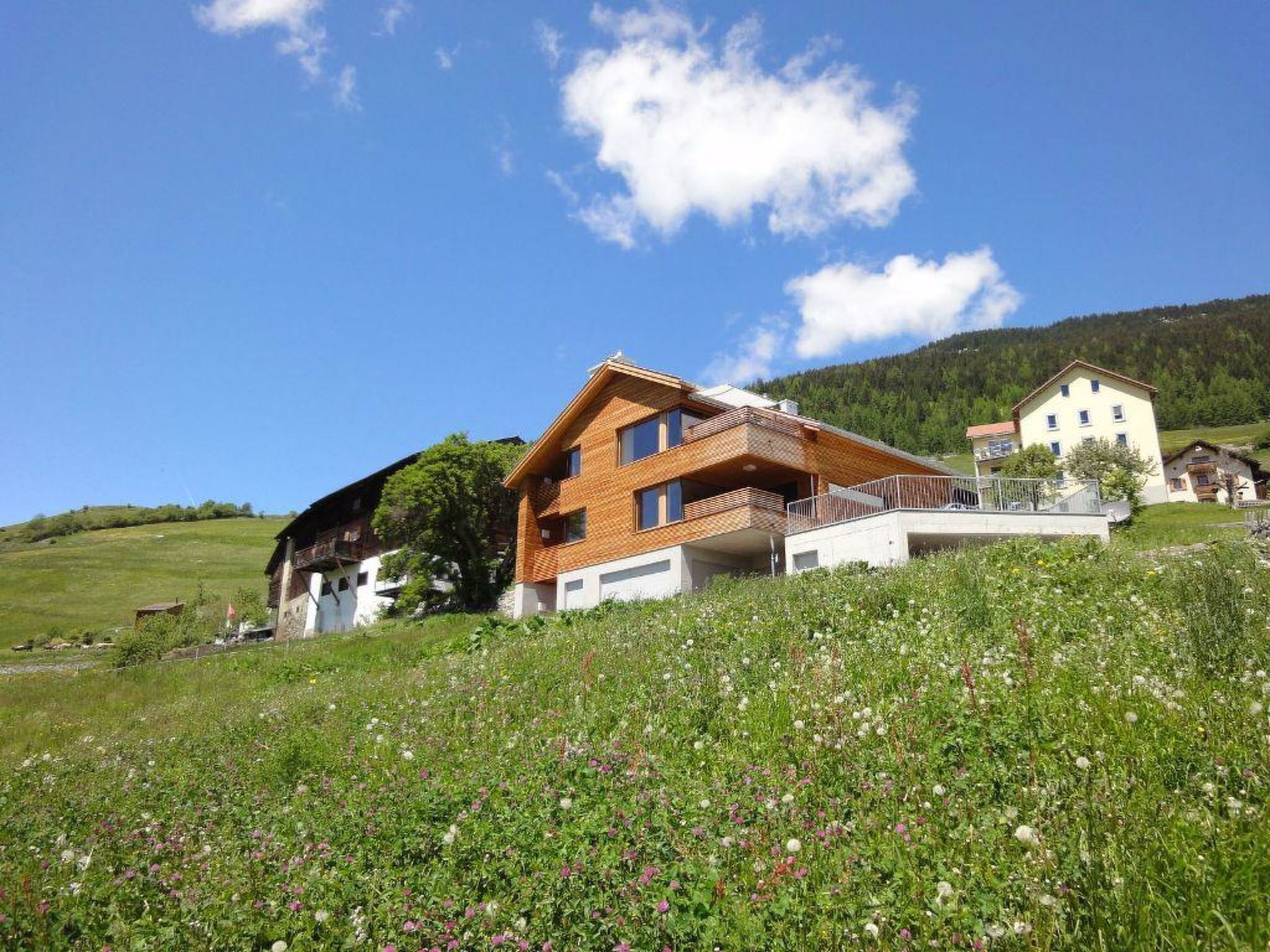 Ein zweistöckiges Haus mit Balkon, umgeben von einem üppigen Grünland und einem Berg im Hintergrund.