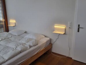 Ein Schlafzimmer mit einem Bett, zwei Wandlampen, einem hölzernen Kopfteil und einer Tür mit Griff.