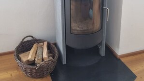 A wood-burning stove with a glass door, a basket of firewood, and a mat on the floor. - Clavo Vigl Appartement/Fewo Clavo Vigl by Interhome (Vaz)