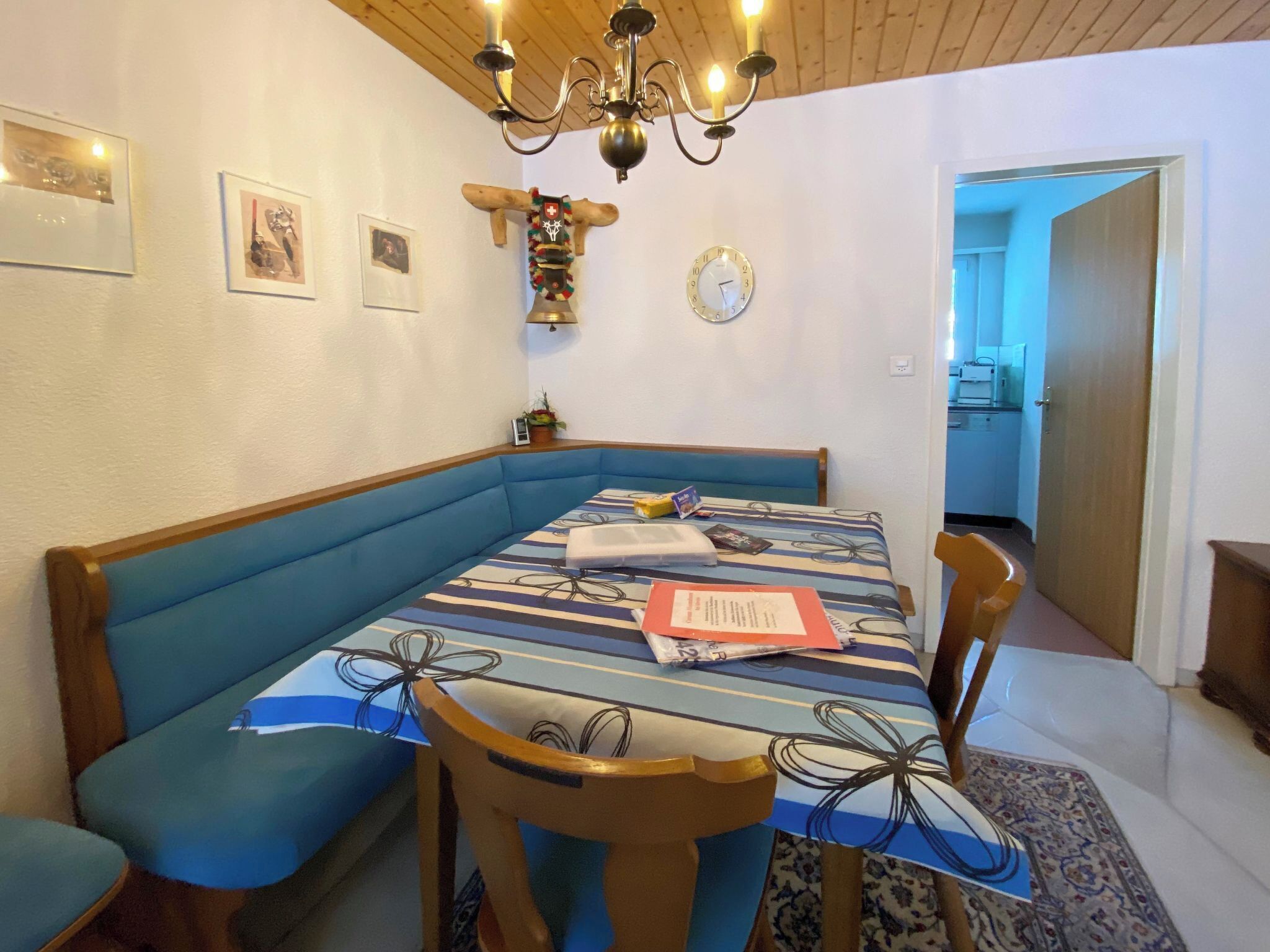 A dining area with a blue bench, a table with a striped tablecloth, and a chandelier.