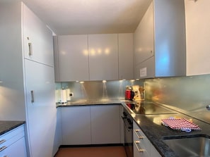 A compact kitchen with white cabinets, a stainless steel sink, and a countertop with a red mug and utensils. - Haus Montana 3/3 Appartement/Fewo,   4-Bettwohnung by Interhome (Lenzerheide)