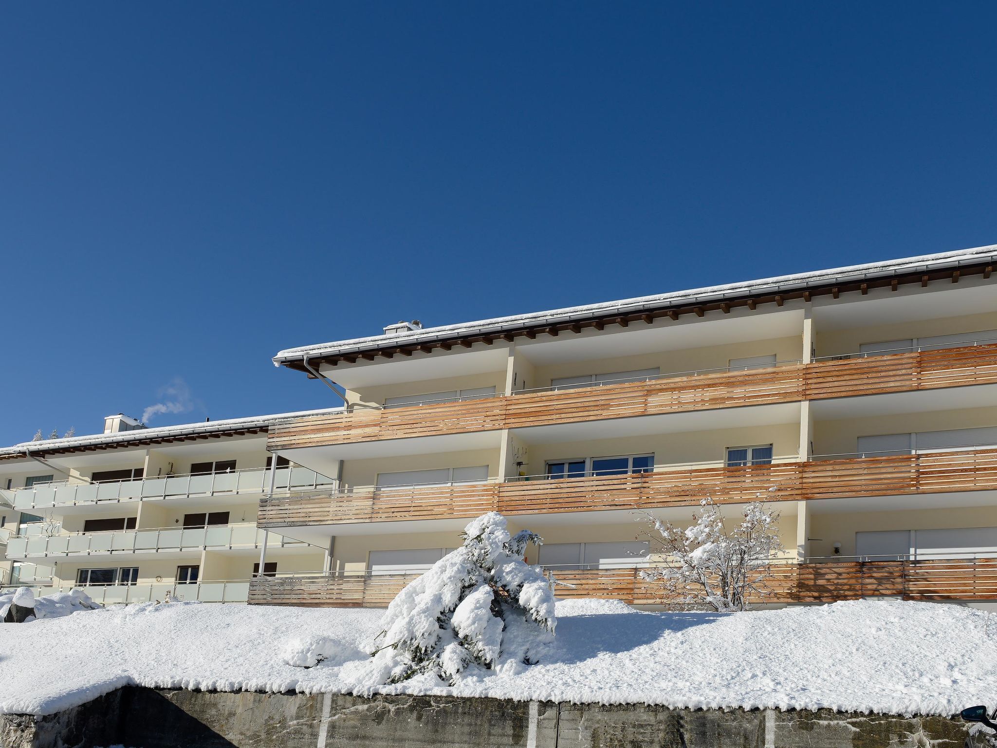 Een meerlaags gebouw met balkons, een met sneeuw bedekte grond en een heldere blauwe lucht.
