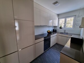 A modern kitchen with white cabinets, a black countertop, and a window with a view of trees. - Ferienwohnung Degen Appartement/Fewo,   Ferienwohnung Degen by Interhome (Valbella)