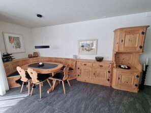 A corner dining area with a round table and chairs, wooden cabinets, and artwork on the walls. - Ferienwohnung Degen Appartement/Fewo,   Ferienwohnung Degen by Interhome (Valbella)
