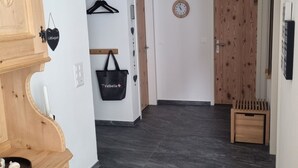 Käytävässä on puinen kaappi, musta laukku, puinen ovi ja seinällä oleva kello.