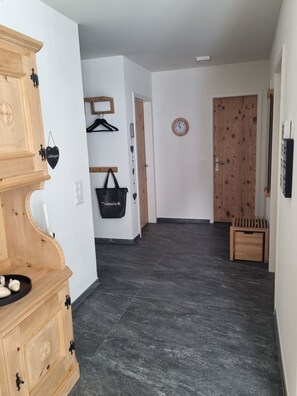 A hallway with a wooden cabinet, a black bag, a wooden door, and a clock on the wall. - Ferienwohnung Degen Appartement/Fewo,   Ferienwohnung Degen by Interhome (Valbella)