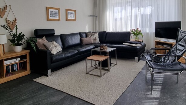 Moderni olohuone, jossa on musta nahkasohva, sohvapöytä, kirjahylly, lattiavalaisin ja televisio.