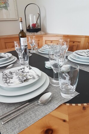 Une table à manger dressée avec des assiettes, des verres et des couverts, une bouteille de vin et un objet décoratif en arrière-plan.