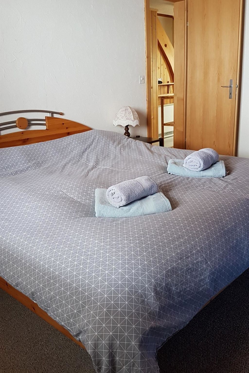 Una cama bien hecha con una colcha de estampado geométrico y dos toallas enrolladas.