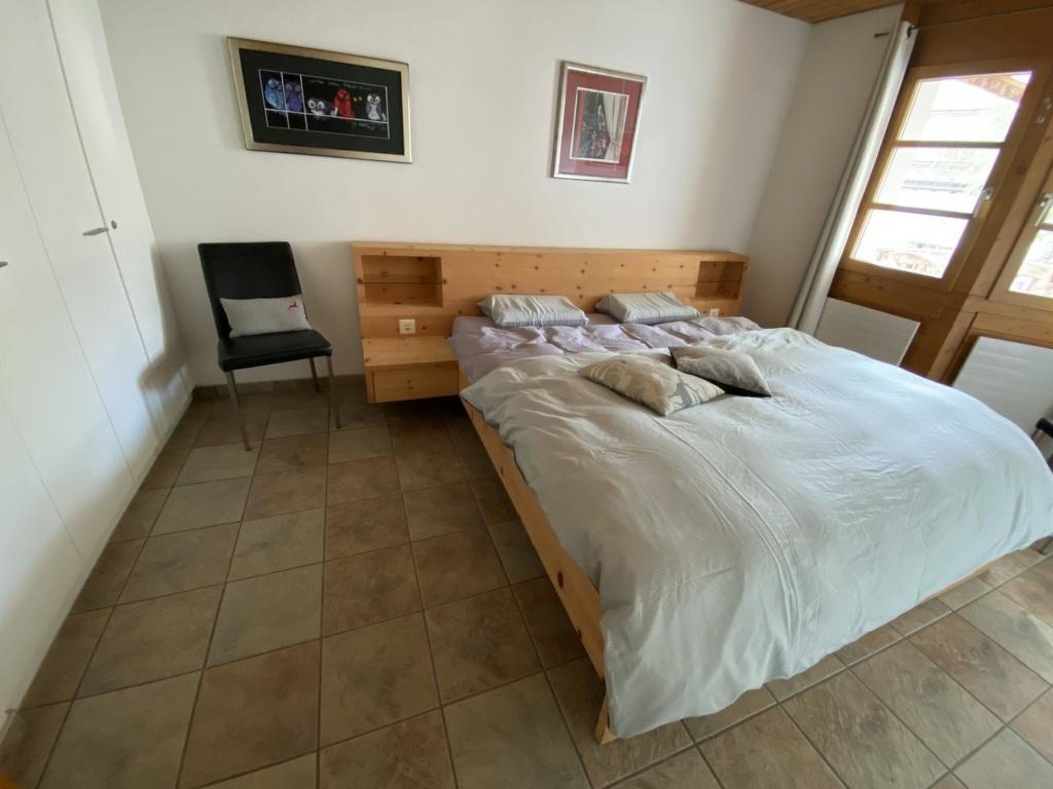 Een slaapkamer met een houten bed, een stoel en een nachtkastje.